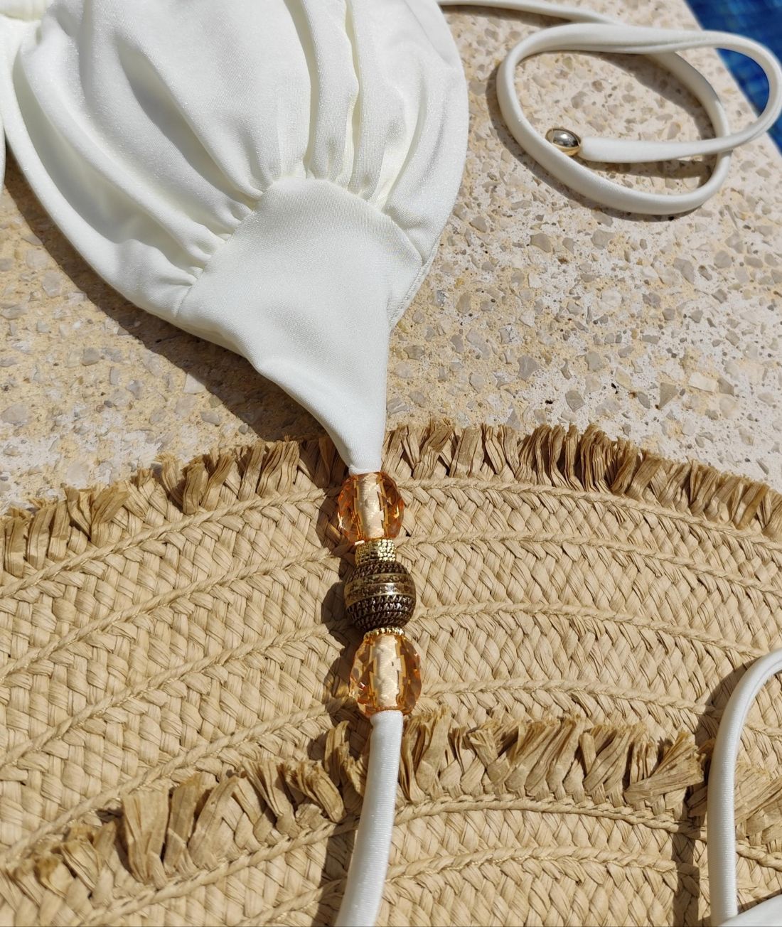 Close-up of white bikini fabric and gold bead detail on straps, premium swimwear finish